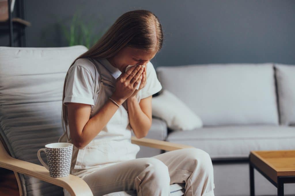 Young woman sits on armchair and coughs